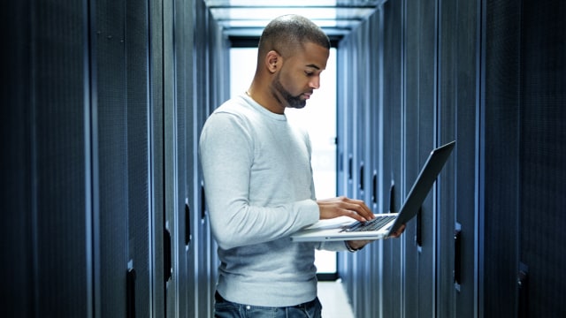 Person mit Blick auf einen Laptop in einem Serverraum
