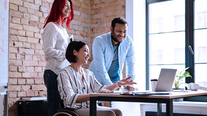 Drei Personen schauen in einem Büro auf einen Laptop