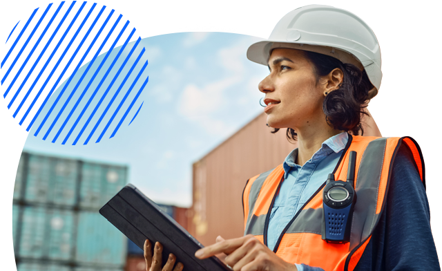 A person holding a tablet, standing in front of shipping containers