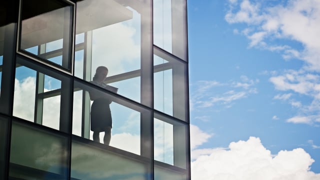 Eine Person arbeitet an einem Tablet am Fenster eines Bürogebäudes